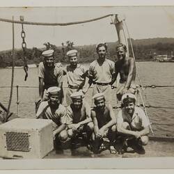 Eight seamen, four standing and four kneeling, on dock of ship
