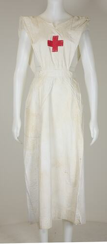 White apron with red cross on front worn by mannequin, front view.