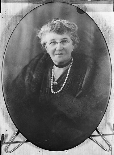 Portrait of elderly woman wearing glasses and a pearl necklace.