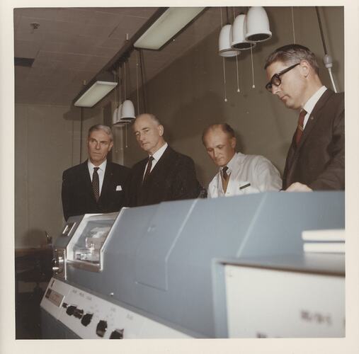 Four men behind large blue machine.