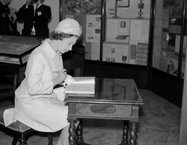 Queen Elizabeth II seated at desk looking through a book.