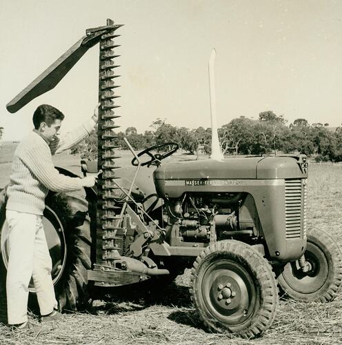 Man posing using a spanner to adjust mid mounted mower on a tractor in a field.