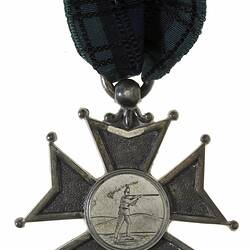 Cross shaped medal suspended from black ribbon. Engraved picture of rifle shooter.