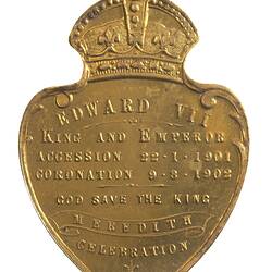 Shield shaped medal with crown atop featuring text in relief.