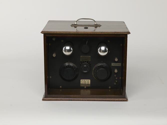 Brown wooden box with top handle. Knobs and dials on side. Front view.