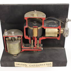 Sectioned Smith's carburettor on black stand with label.