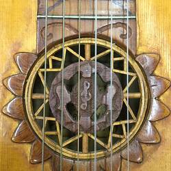 Detail of decorative brown wooden mandolin sound hole and strings. Treble clef in centre.