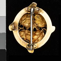 Back of round gold brooch with vertical pin.