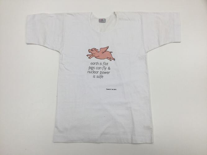 White t-shirt with printed pink cartoon pig with wings over black text.