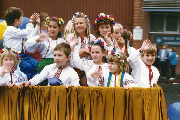 Group of children on a street procession float, waving and wearing Ukrainian national dress.