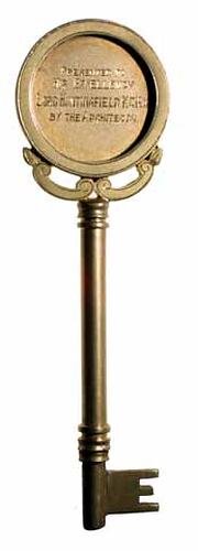 Decorative brass key with disc shaped handle bearing inscription.