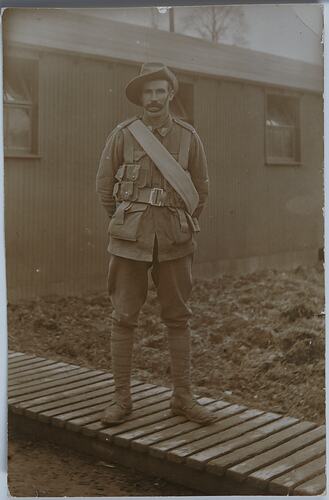 Front of postcard with soldier standing on duckboard.