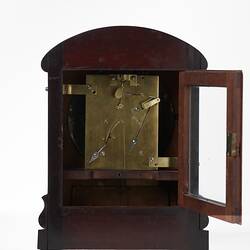Back of mantel clock. mahogany case. Small glass door open shows internal mechanism.