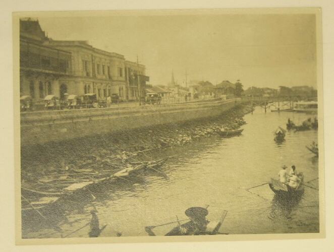 vehicles on road running next to river where people rowing boats.