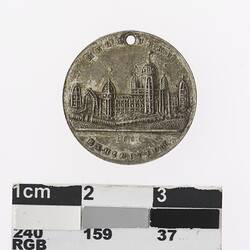 Round silver coloured medal with building, text above and below.