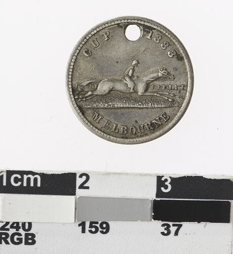 Round silver coloured medal with man on horseback in full stride and text surrounding.