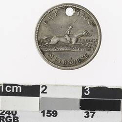 Round silver coloured medal with man on horseback in full stride and text surrounding.