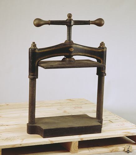 Small leather press with turning handle at top.