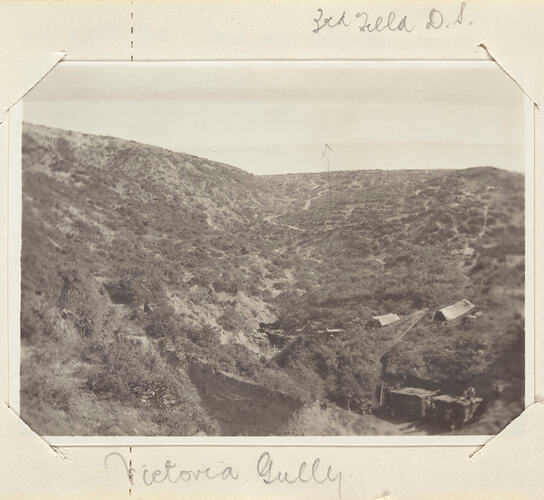 Sloping, scrub covered landscape with two tents and truck on the right bottom side.
