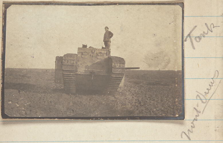 Serviceman standing on the wheel of a tank in a field.
