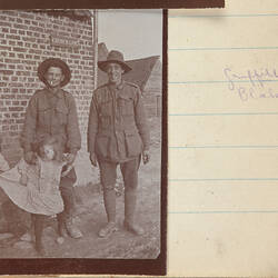 Two servicemen and two young girls standing by brick wall.