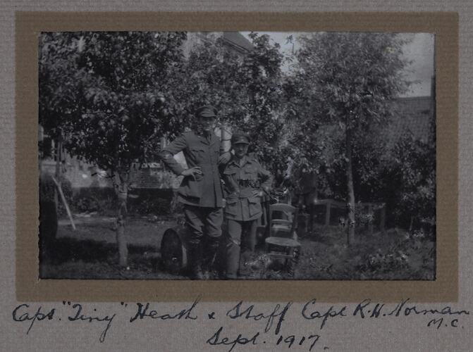 Three men in military uniform in a garden with trees and house in background.