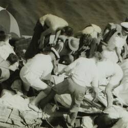 View from above of a lifeboat with multiple people bending down to assist wounded people covered in sheets.