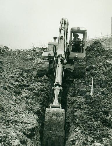 Man operating a crawler excavator digging a trench.