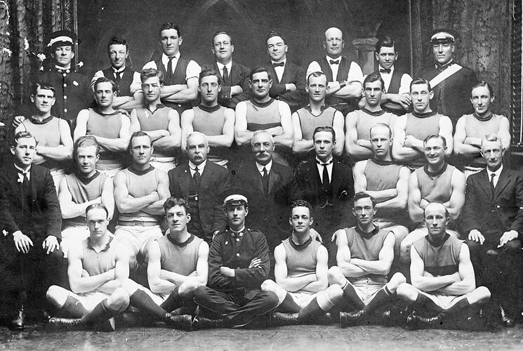 Group portrait of football players and officials positioned in four rows, seated and standing.