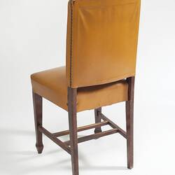 Yellow furnished chair with dark wood legs, back.