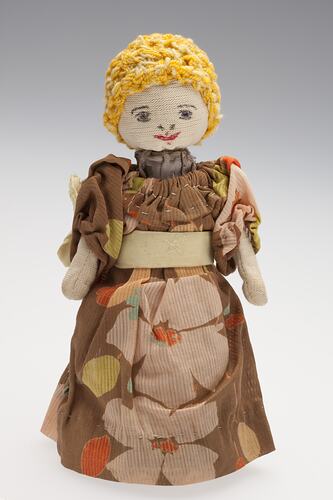 Cone-shaped cotton female doll with yellow hair. Wears a brown dress with yellow flowers.