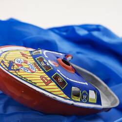 Brightly coloured little metal speedboat toy on blue fabric.