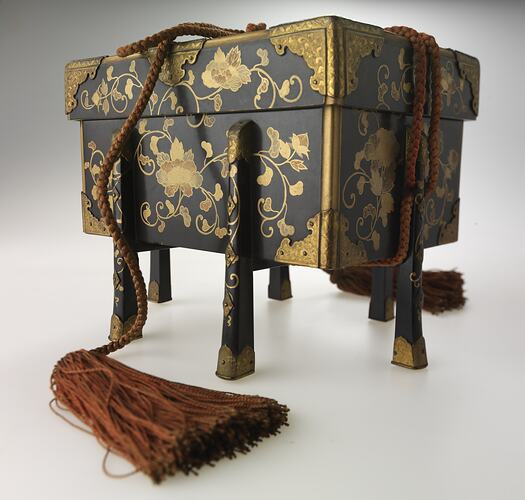 Lidded decorated, four-legged box with tassled ties.