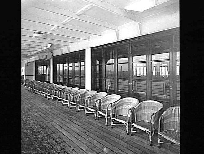 Ship deck. Round cane arm chairs at right.