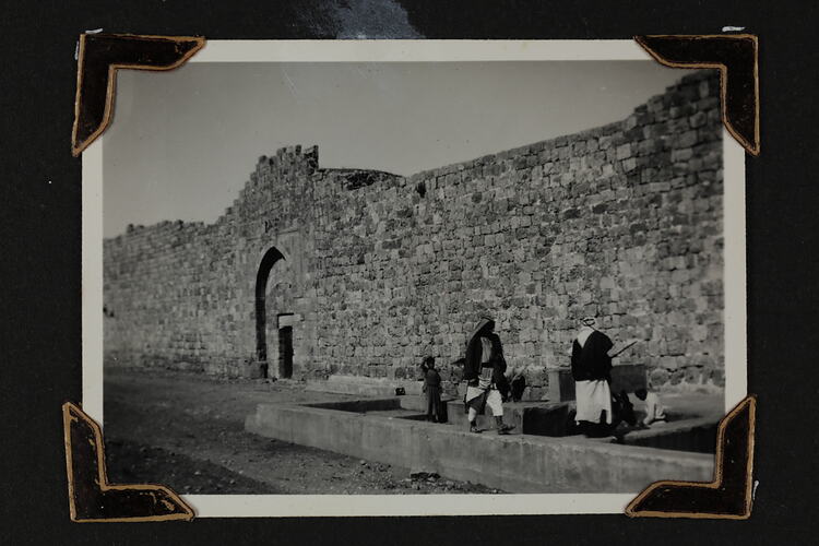 Small group of people by a stone wall and archway.