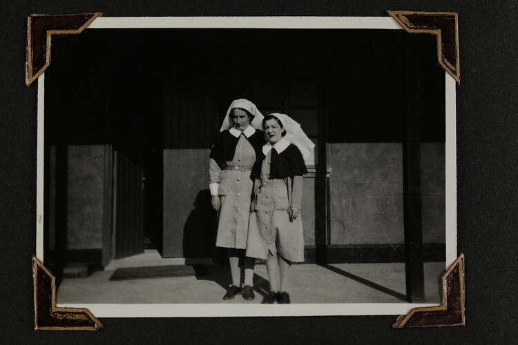 Two woman in nurses uniform standing in front of a building.