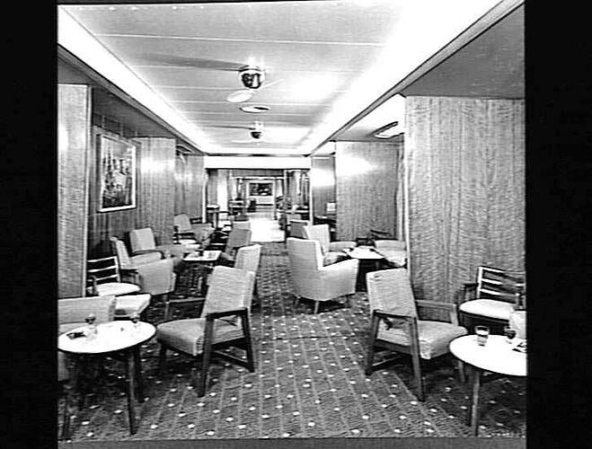 Ship interior. Narrow room with upholstered chairs and armchairs around tables.
