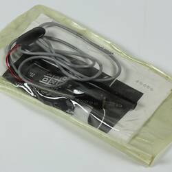 Black pen with grey cable attached and folded white page with black printing in plastic sleeve.