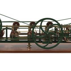 Paper making machine miniature model made of metal. Two larger wheels joined by belts. Copper drum at one end.