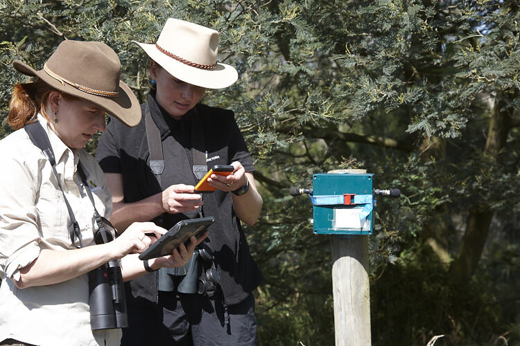 Two women in hats look carefully at some scientific equipment.