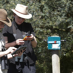 Two women in hats look carefully at some scientific equipment.