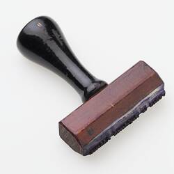 Red-brown wooden stamp with black handle.