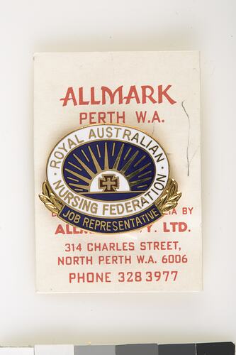 Enamel blue and white oval badge attached to white card with red printing.