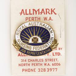 Enamel blue and white oval badge attached to white card with red printing.