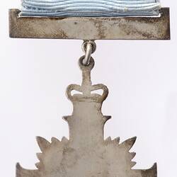 Back of metal cross medal suspended from white ribbon.