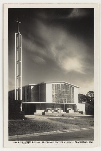 Exterior of white church with large central rectangular glass. White cross on metal tower at left.