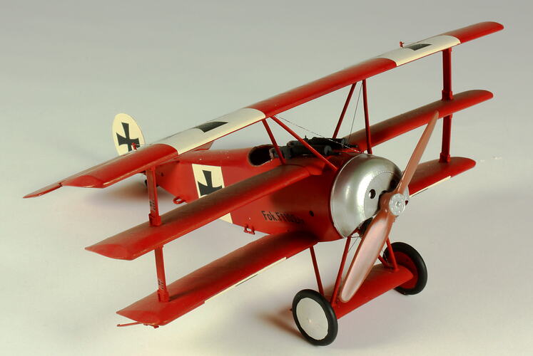 Red aeroplane model. White strip on top of wings with black cross. Right three quarter front view.