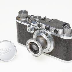 Black leather and silver metal bodied camera. Silver lens at front and dials, buttons on top.