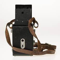 Metal reflex camera. Body covered in black leather. Leather carry strap. Back view.