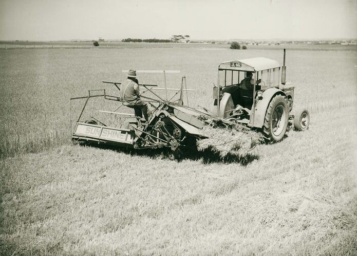 Man driving a tractor towing a PTO Reaper Binder with a man operating it.